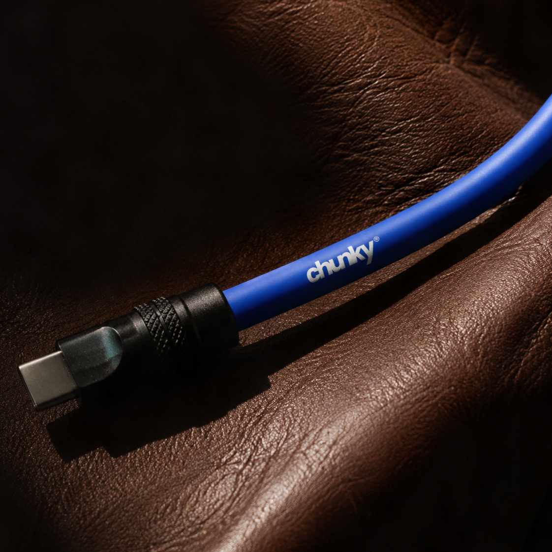 A close-up of a blue USB-C cable with a black connector, branded with the white 'chunky' logo, resting on a textured brown leather surface.
